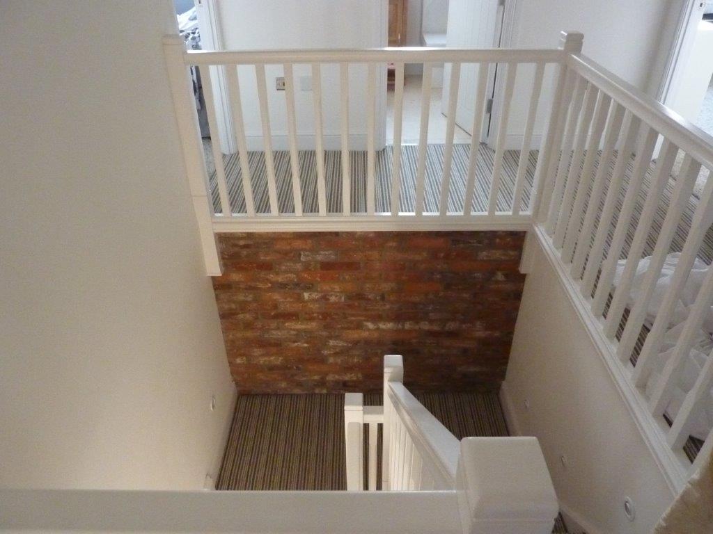 Stairwell with white railing and brick wall. View from above, carpeted stairs.