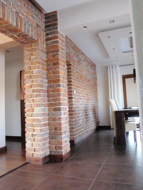 Interior brick wall and support beams, brown tiled floor, and dining area with white curtains.