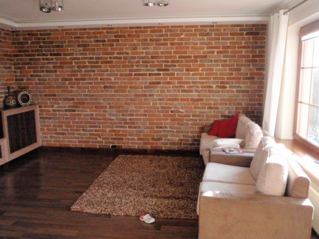 Living room with exposed brick wall, beige sofa, rug, and dark wood flooring.