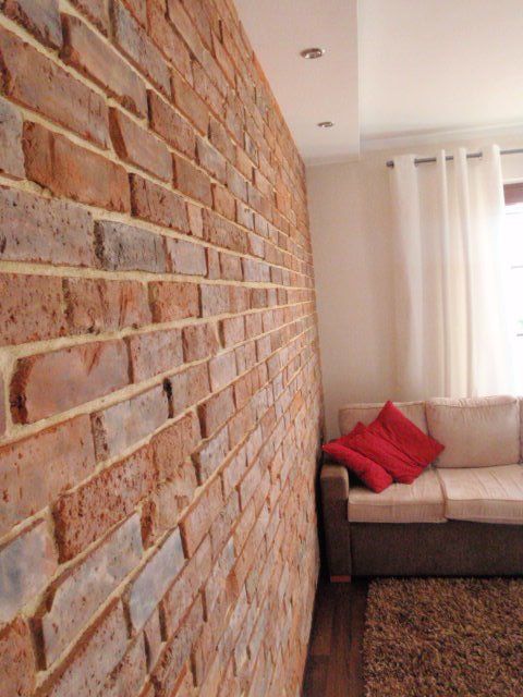Brick wall in a living room next to a beige sofa with red pillows and white curtains.