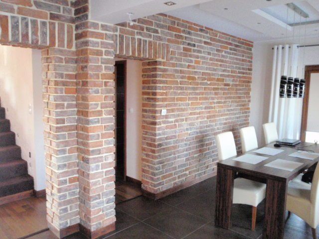 Brick accent wall in a dining room with dark wood table and white chairs; archway entrance.