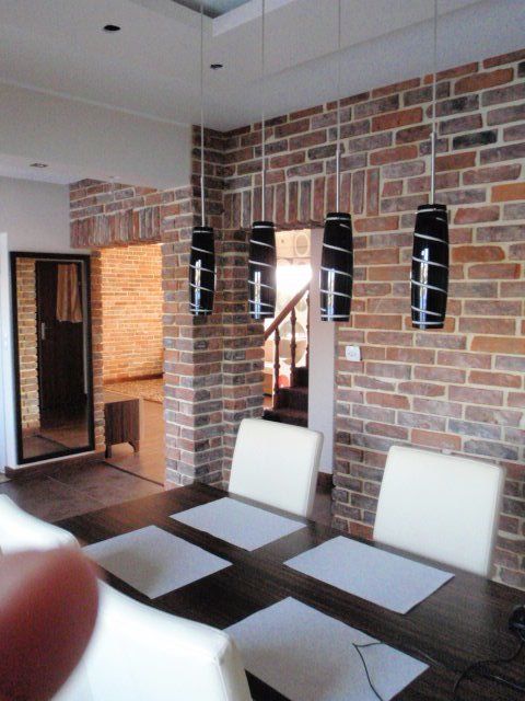Dining room with brick wall, modern black pendant lights, and white chairs at a dark wood table.