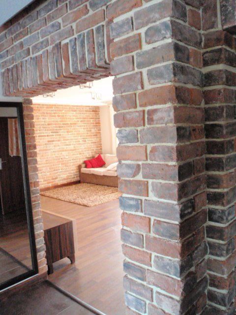 Brick doorway leading to a room with a sofa and rug; brown and red tones.