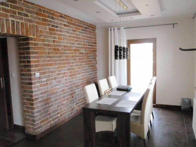 Dining room with brick wall, dark wood table and chairs, and a doorway with white curtains.