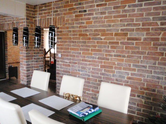 Dining room with brick walls, dark wood table, white chairs, and hanging black light fixtures.