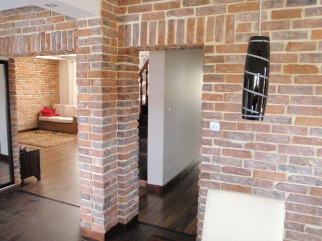 Interior with brick walls and archways, dark wood floors. A light fixture hangs on the right.
