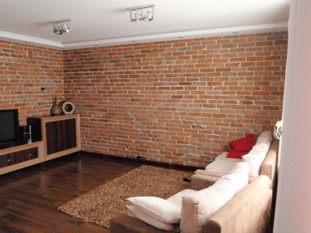 Living room with exposed brick wall, wood floor, beige couch, and television.