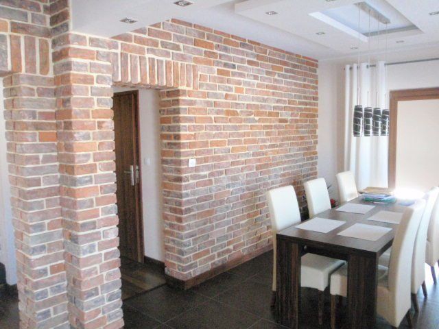 Brick wall in dining room with dark table, white chairs, and wooden door.