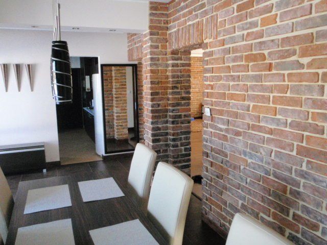 Dining room with brick accent walls, dark wood table, white chairs, and modern light fixture.
