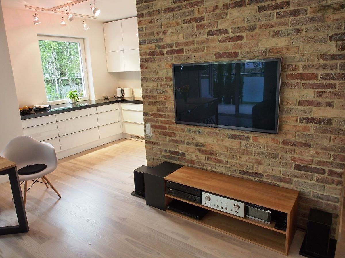 Living room with exposed brick wall, TV, wooden media console, and kitchen visible in the background.