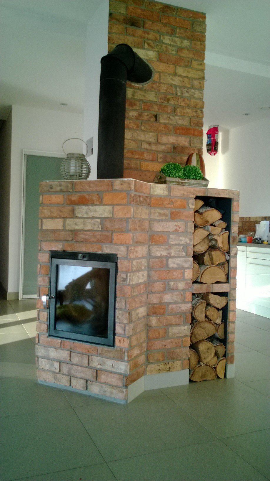 Brick fireplace with black stovepipe, firewood storage, and a glass door.