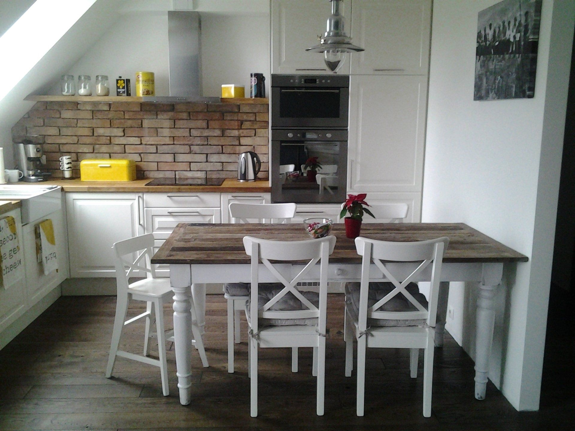 Kitchen with white cabinets, exposed brick backsplash, and a wooden dining table with four white chairs.