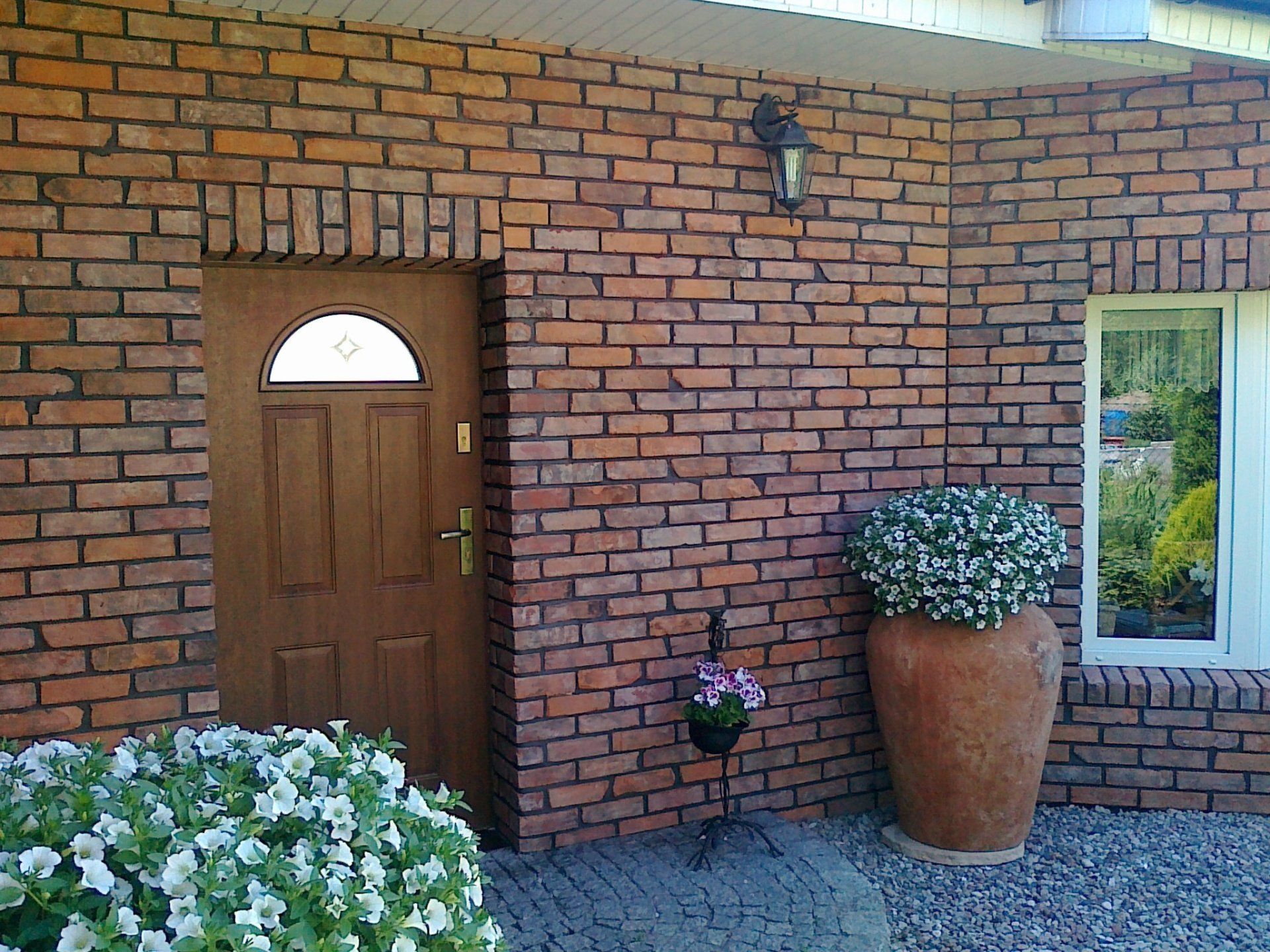 Brick facade with brown door, window, and large terracotta pot with petunias.