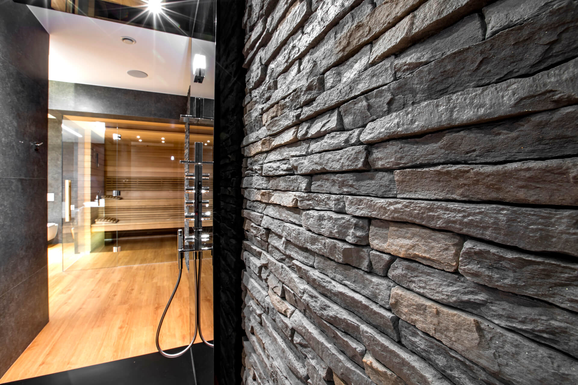 Stone accent wall in a bathroom, with a wooden floor and glass shower.