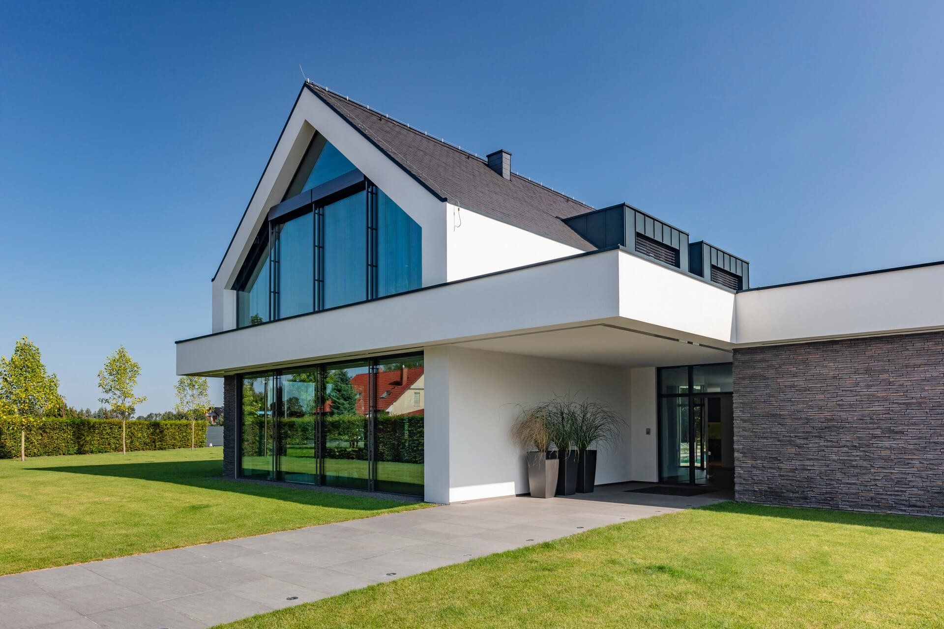 Modern white house with dark roof and large windows, on a grassy lawn under a blue sky.