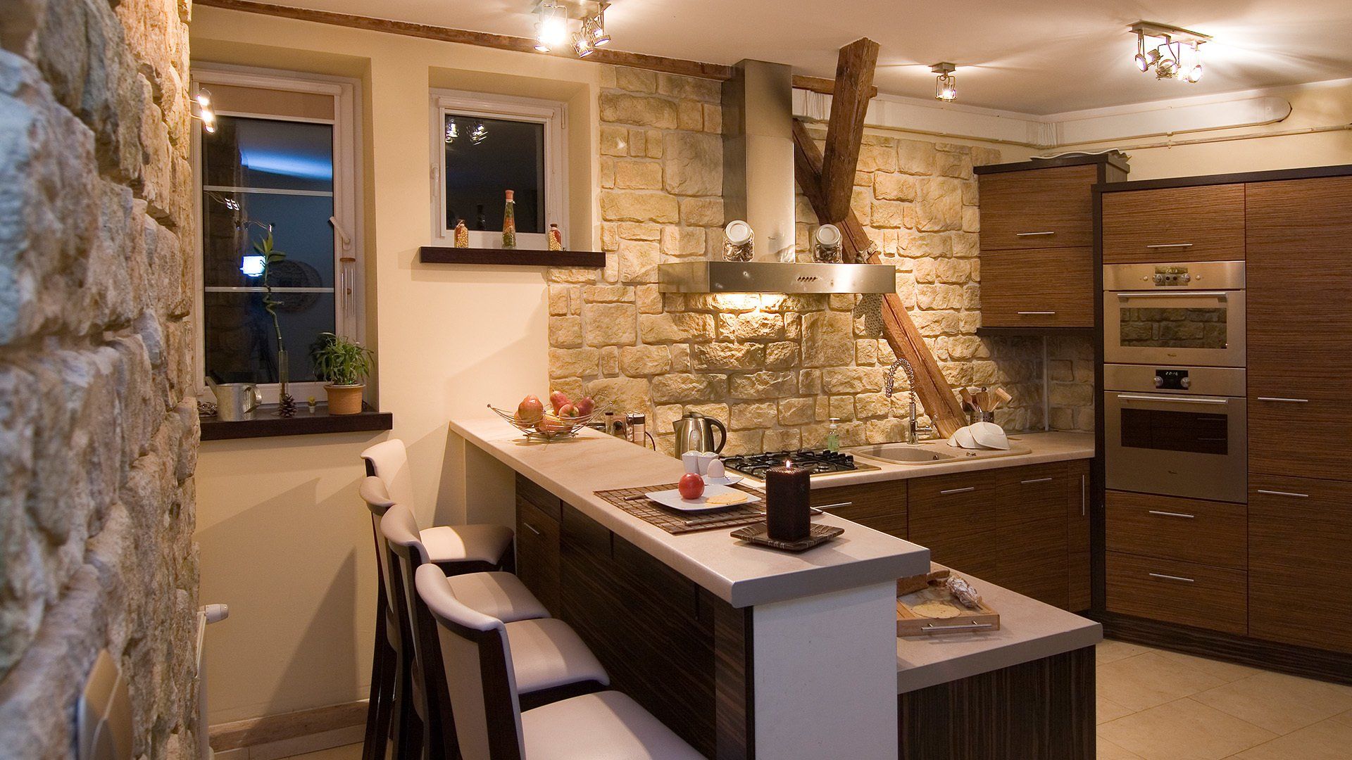 Kitchen with stone wall, wooden cabinets, breakfast bar, and stainless steel appliances.