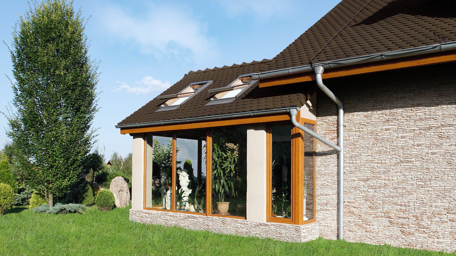 Sunroom with brown trim and roof, connected to stone-walled house, green yard and sky visible.