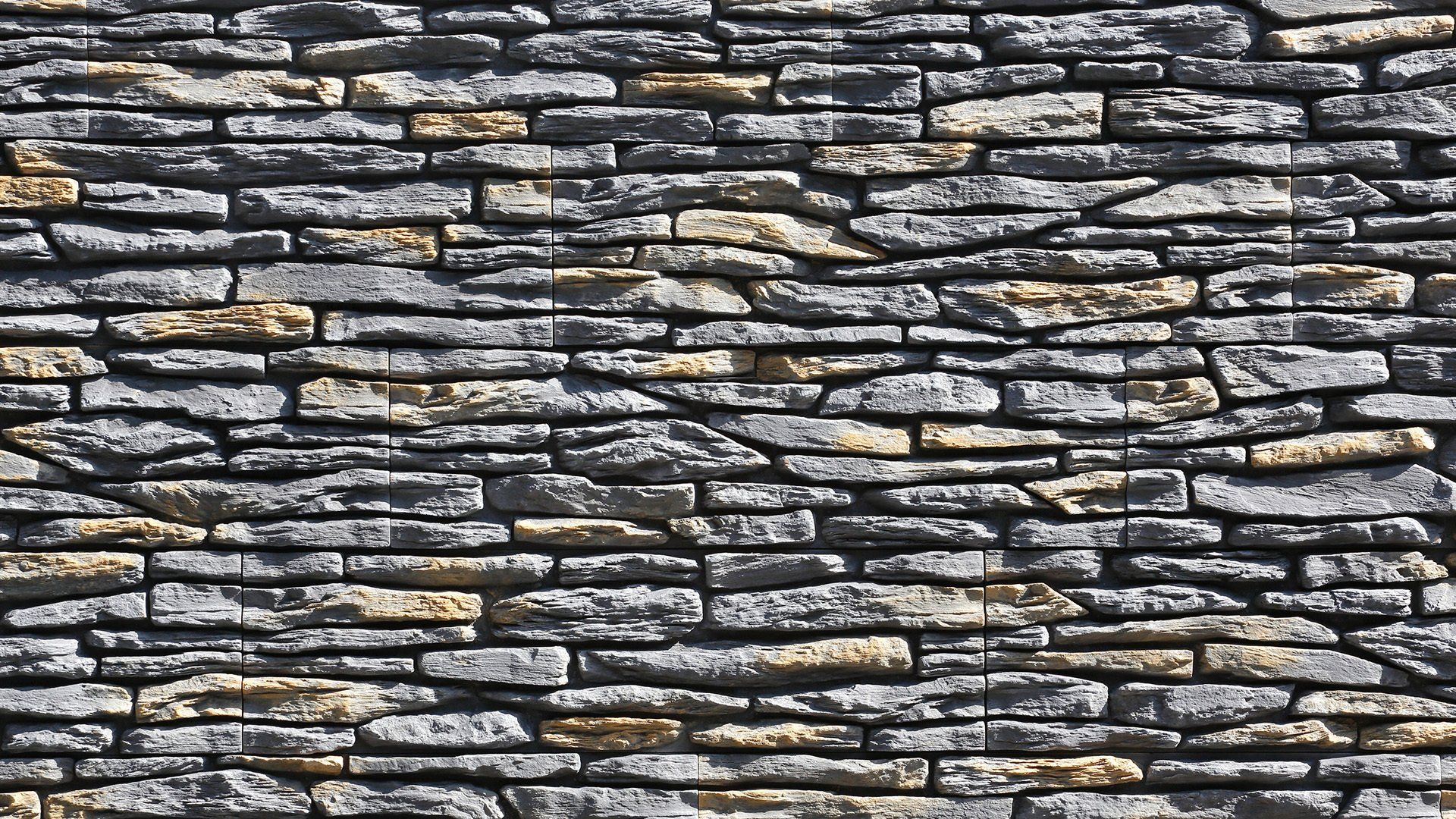 Gray and tan stone wall with rough, irregular texture.