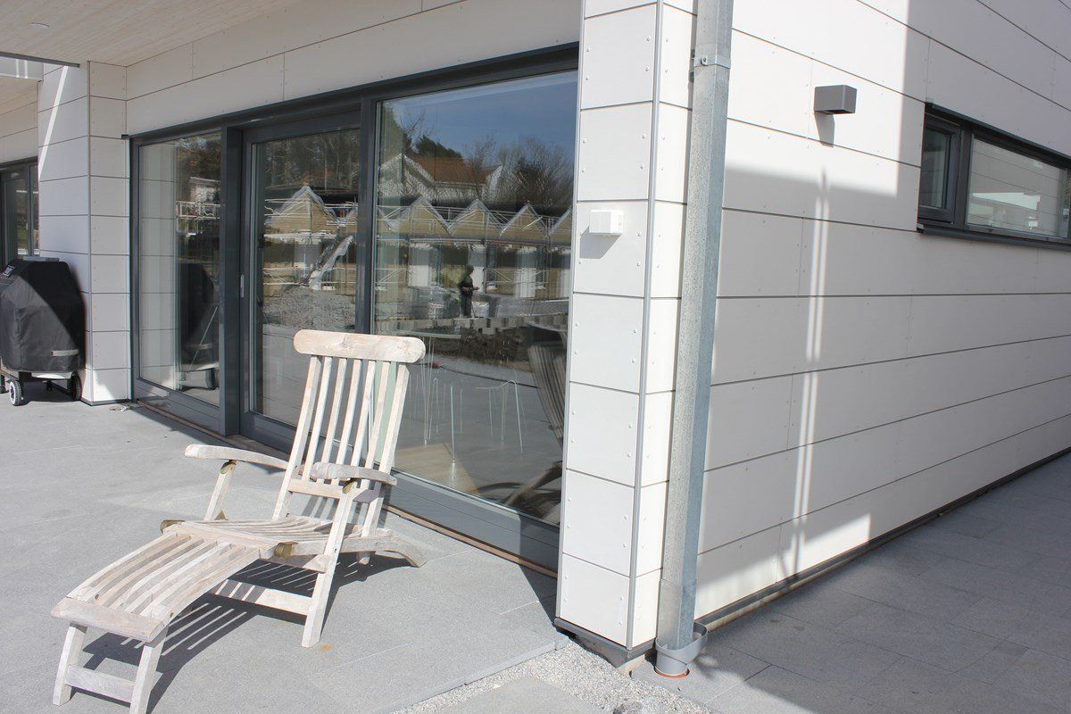 Wooden chair on a gray patio next to a building with large windows reflecting a neighborhood.
