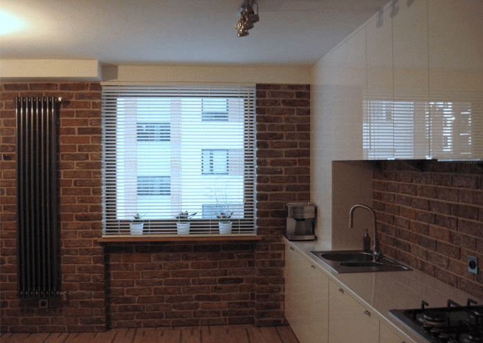 Kitchen with brick walls, a window with blinds, and white cabinets. A radiator is to the left.