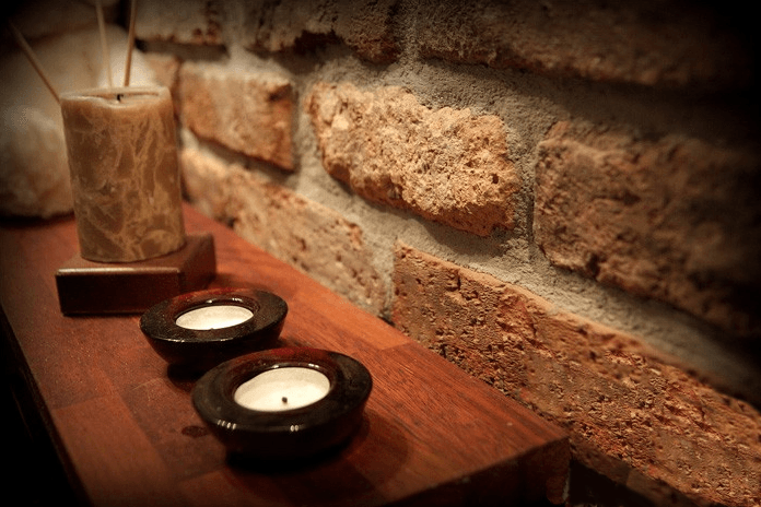Candles on a wooden shelf next to a brick wall.