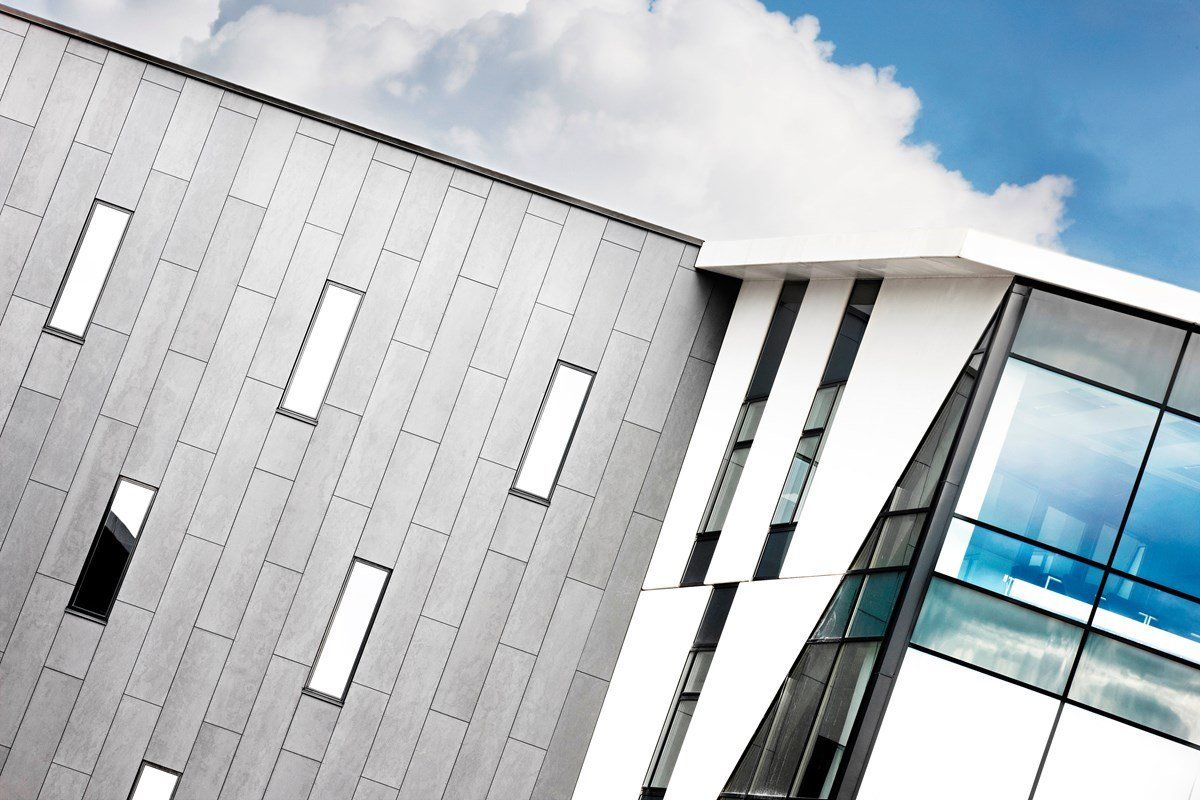 Modern building with gray and white facade and glass windows against a cloudy sky.