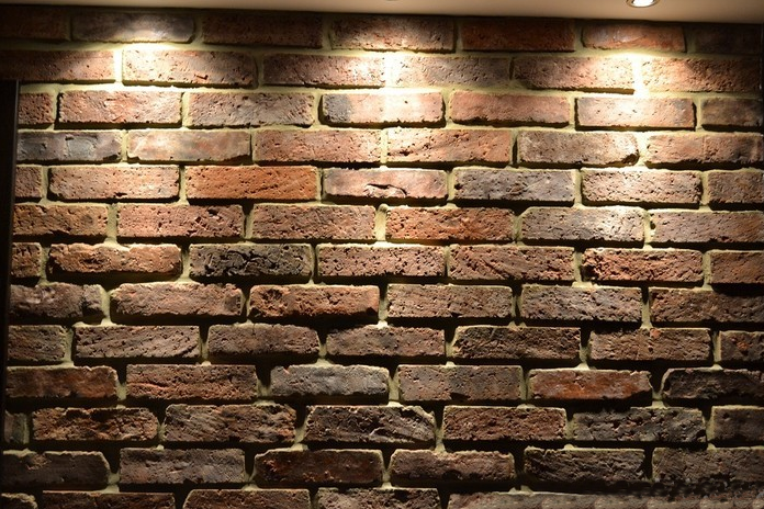 Brick wall with various shades of brown and dark gray, illuminated by overhead lighting.