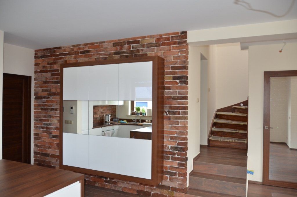 White cabinets on a brick wall in a kitchen, next to stairs and a doorway.
