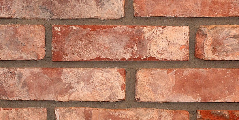Red brick wall, weathered with light-colored patches, grey mortar between bricks.