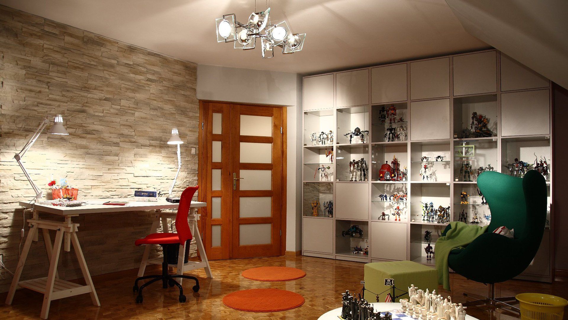 A brightly lit, modern home office with a desk, shelves displaying collectibles, and a green accent chair.