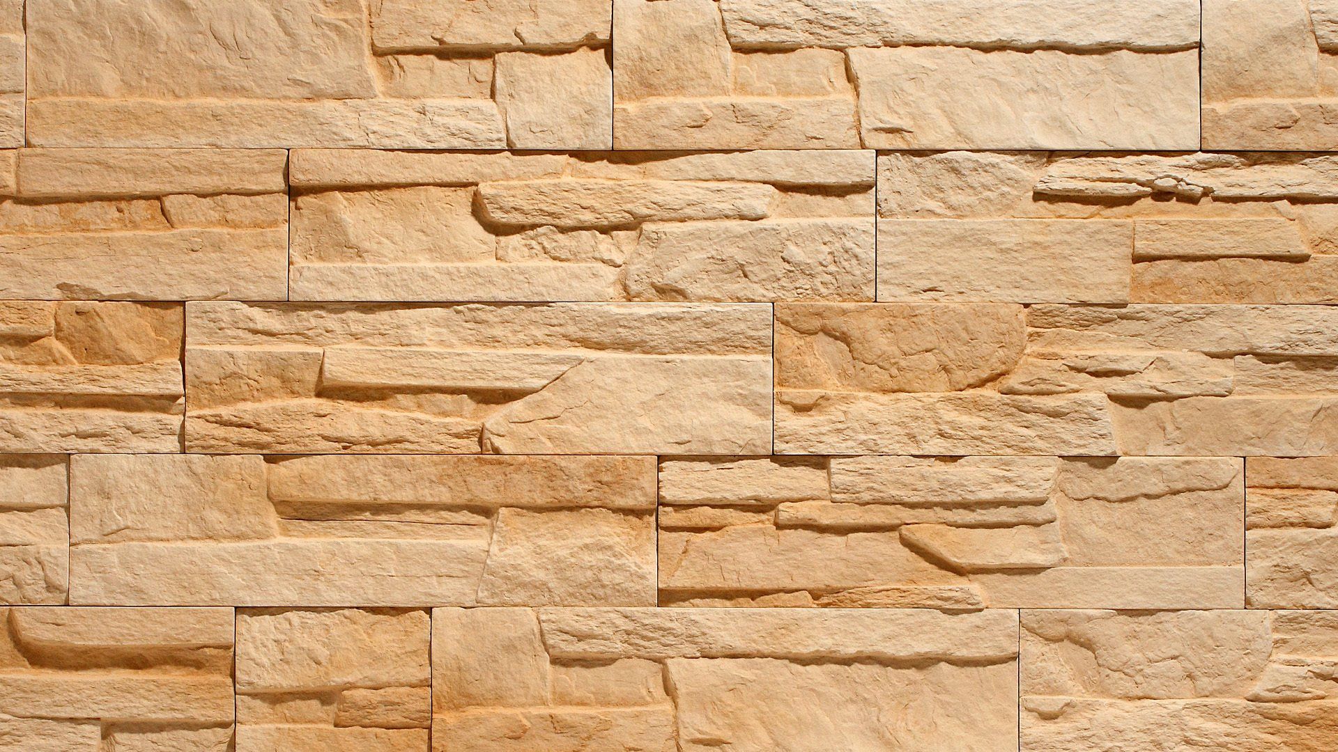 Rough, light-brown stacked stone wall with varying depths and textures.