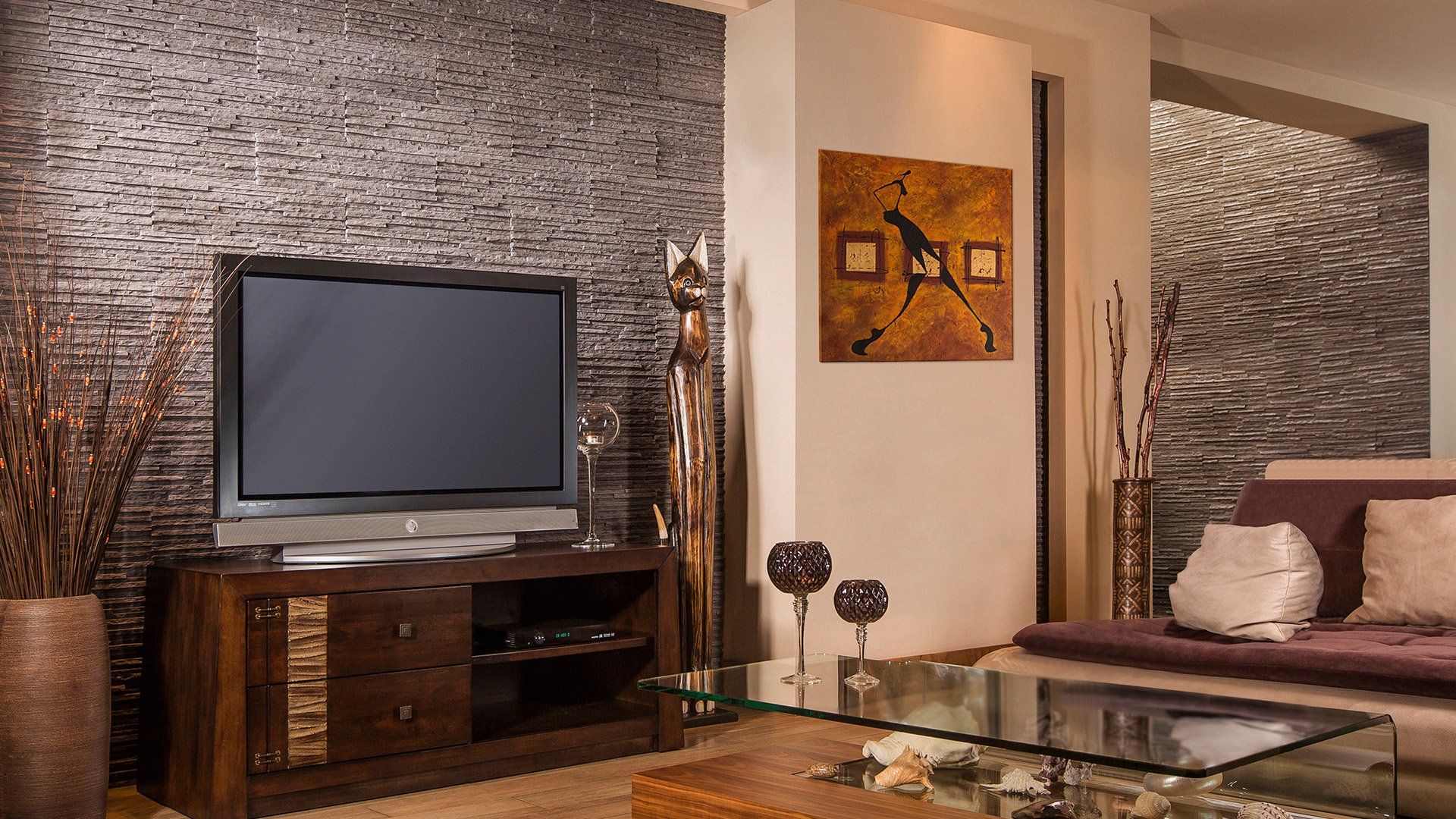 Living room with TV on wooden cabinet, metallic accent wall, sofa, artwork, and glass coffee table.