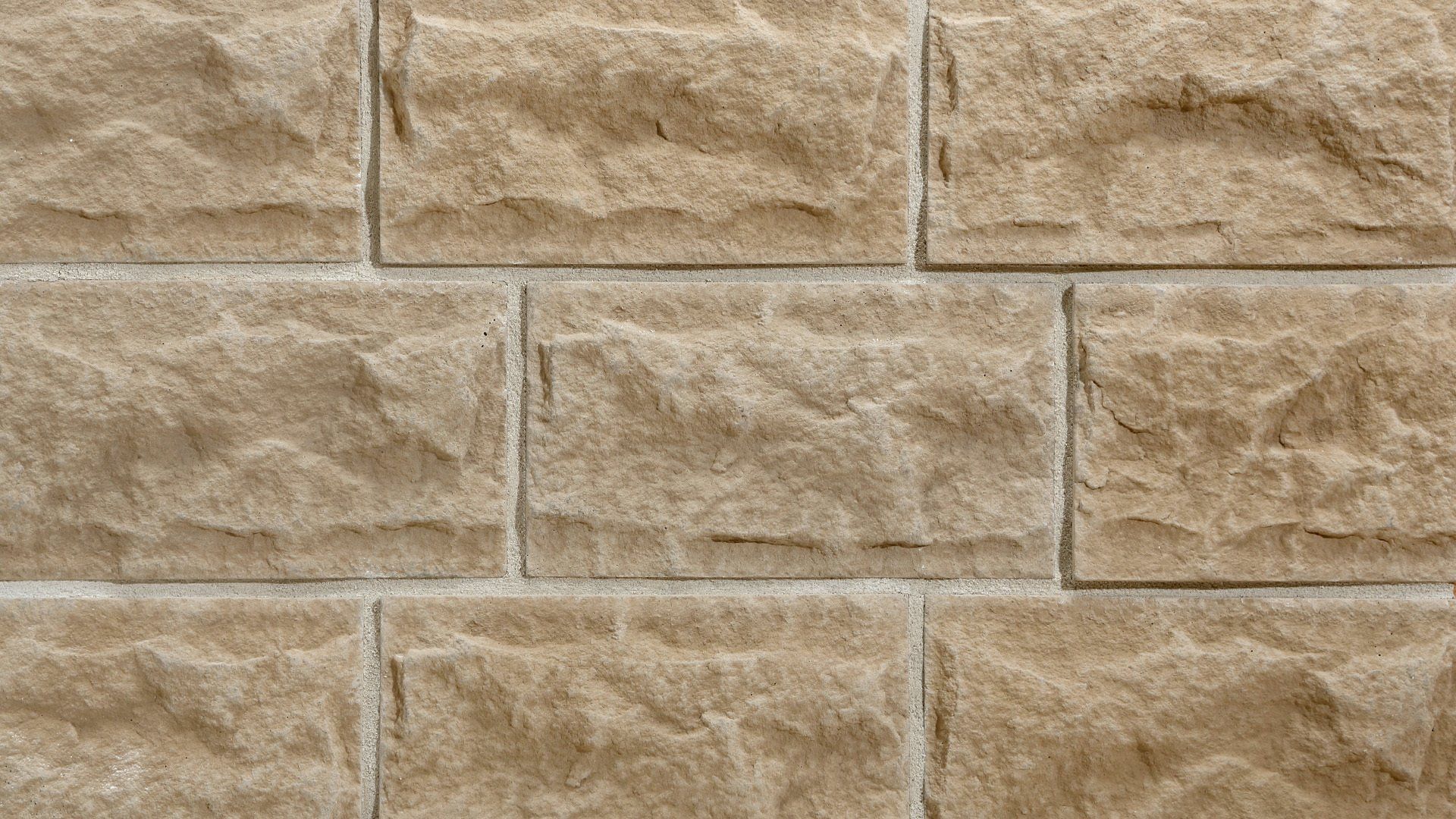 Close-up of a beige brick wall with textured rectangular blocks and light gray mortar.