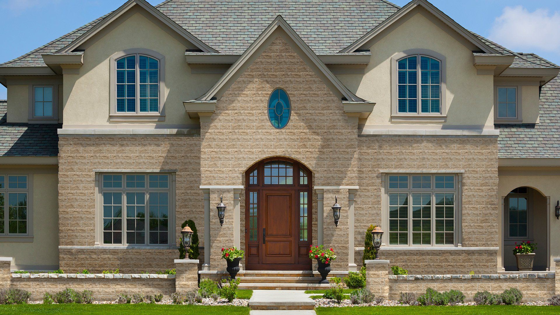 A two-story house with tan brick facade, arched windows, and a brown front door.