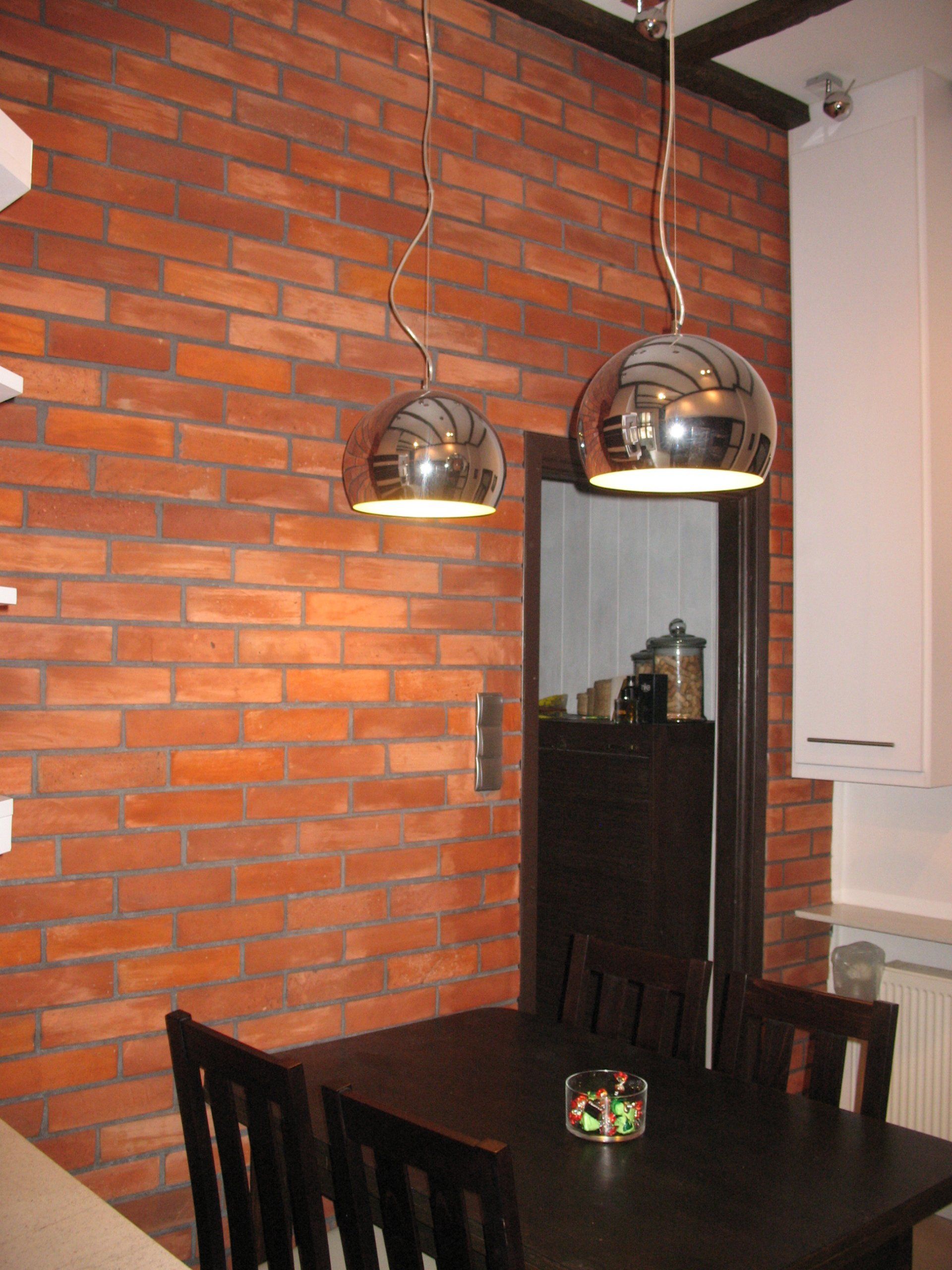 Dining area with exposed brick wall, dark wooden table, black chairs, and two spherical pendant lights.