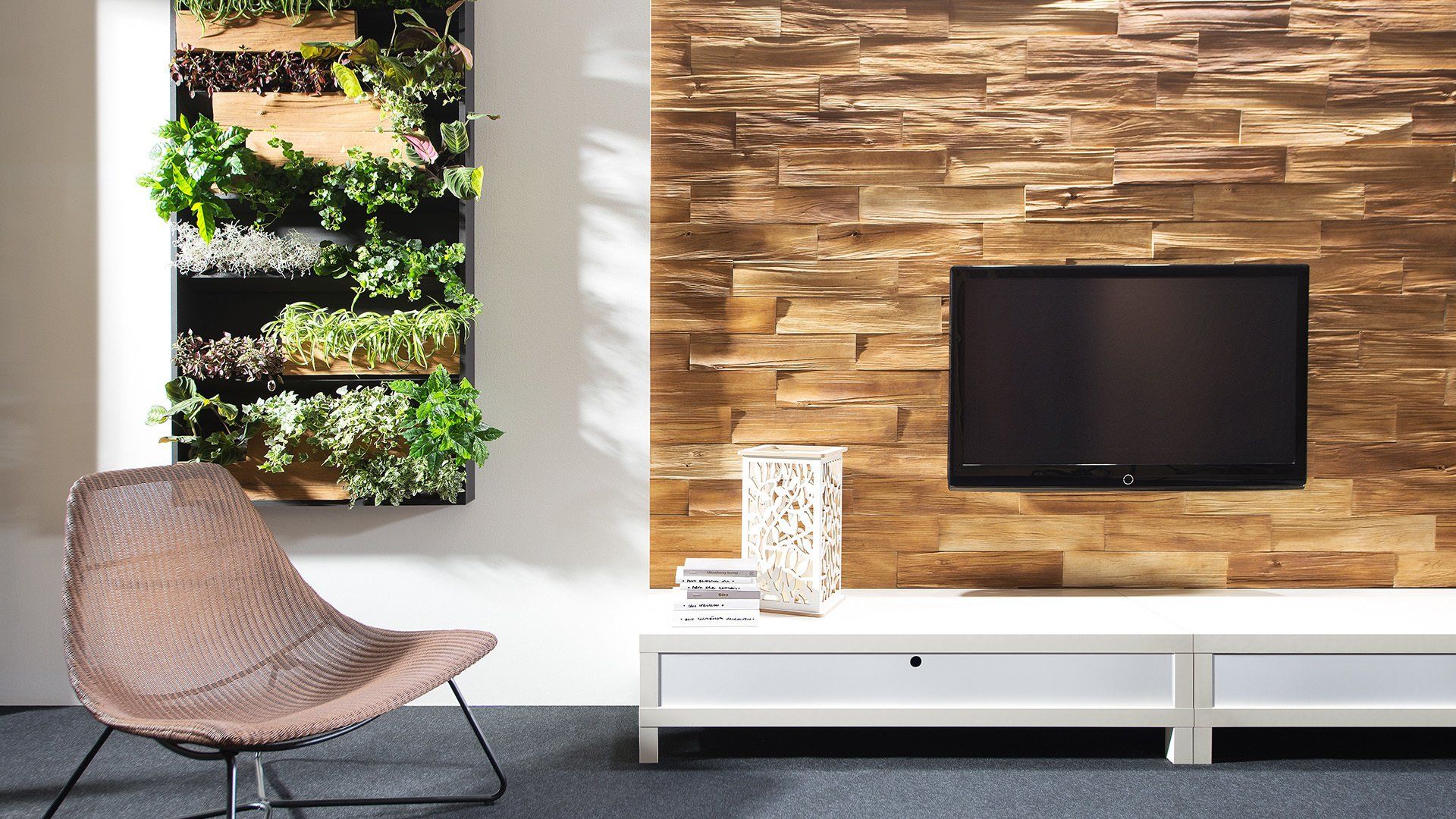Living room with a stone wall and a television, a white cabinet, a green wall of plants, and a woven chair.