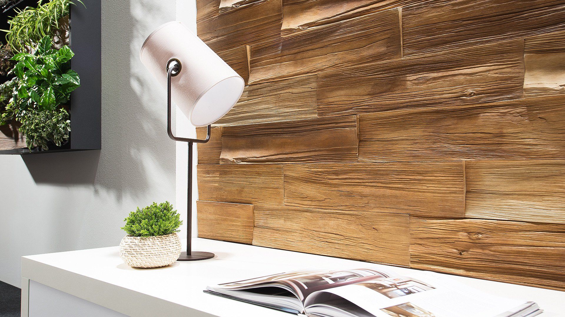 A modern desk with lamp and plant in front of a textured wood wall.