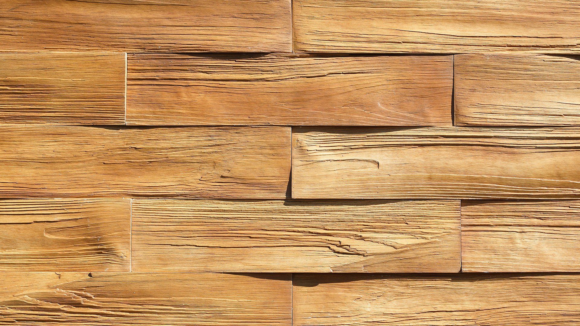 Close-up of a wall made of rectangular, textured, beige and brown stone tiles arranged in a stacked pattern.