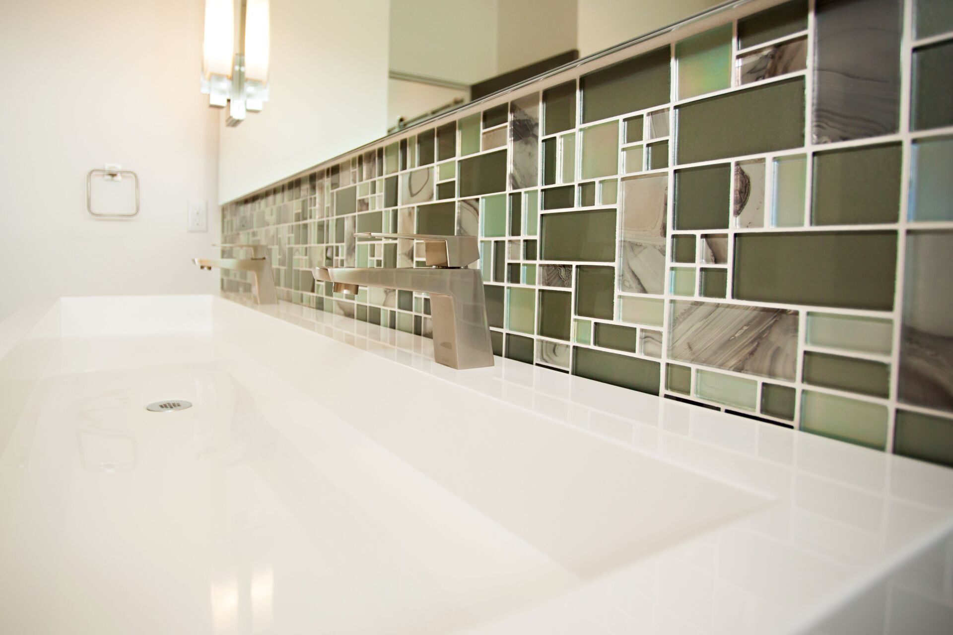 A bathroom sink with green and white tiles on the wall