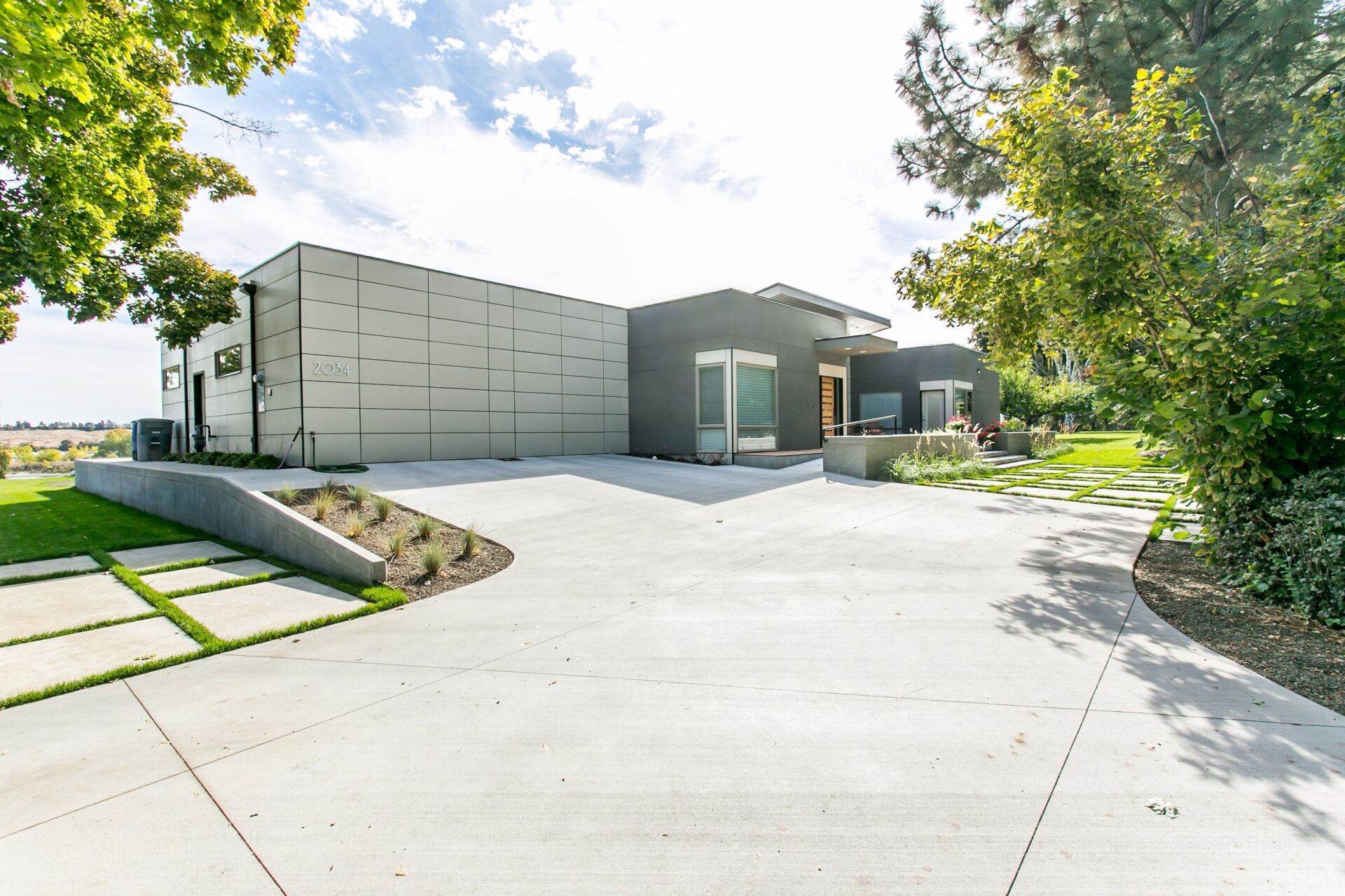 A large modern house with a concrete driveway leading to it.