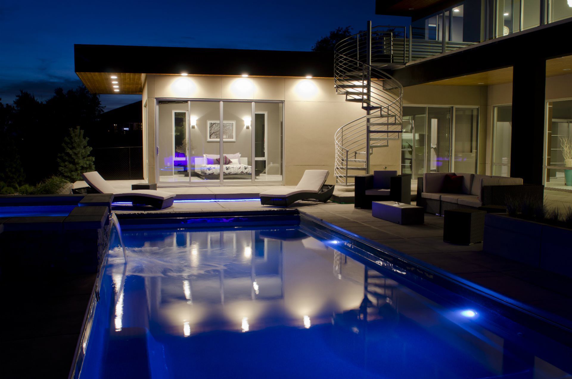 A large swimming pool is in front of a house at night.