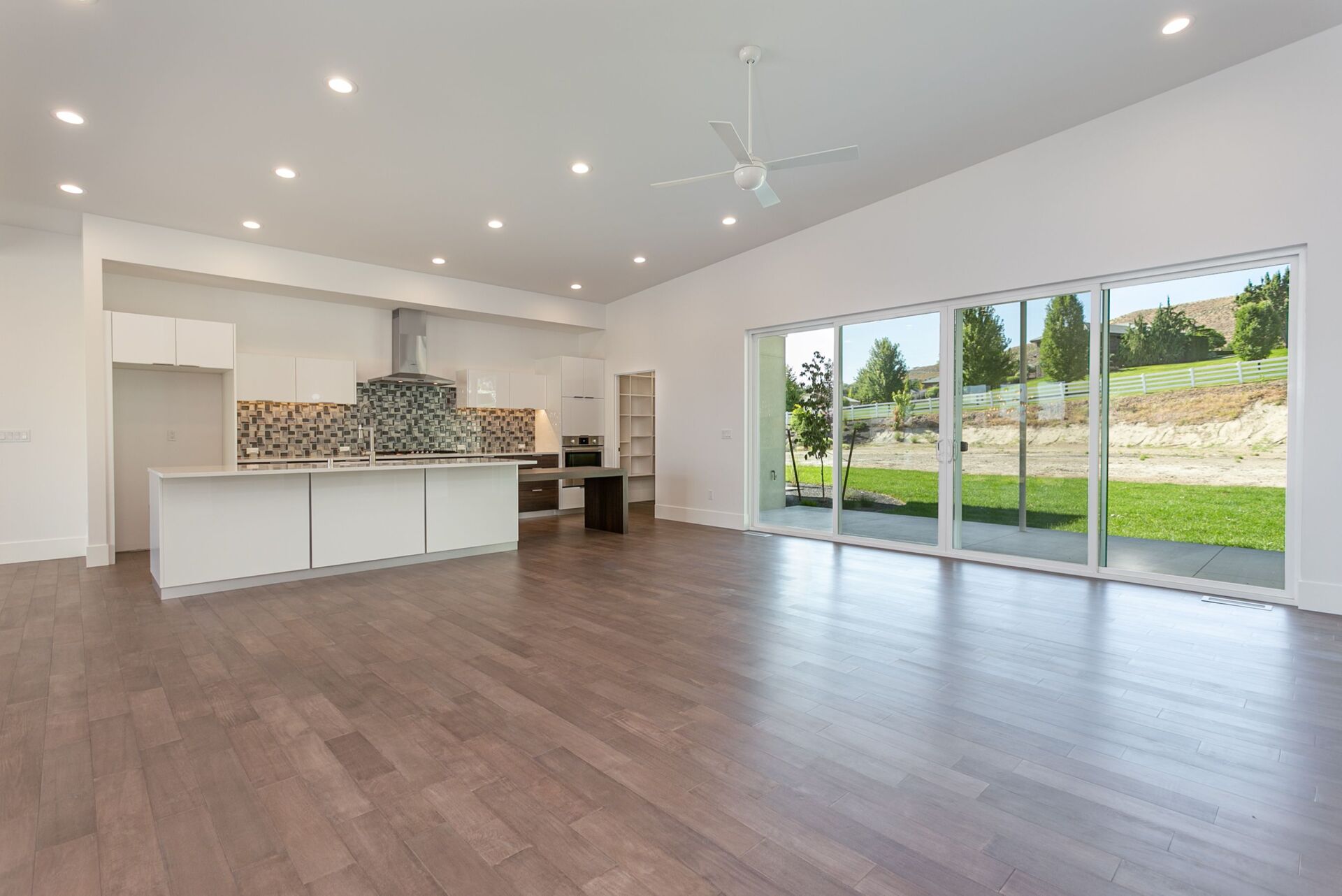 An empty living room with hardwood floors and sliding glass doors leading to a kitchen.