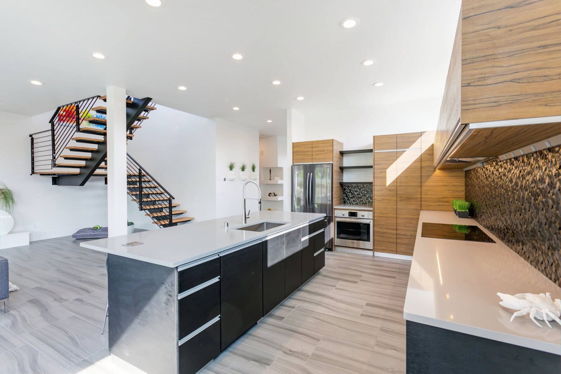 A kitchen with a large island , stainless steel appliances , wooden cabinets and a staircase.