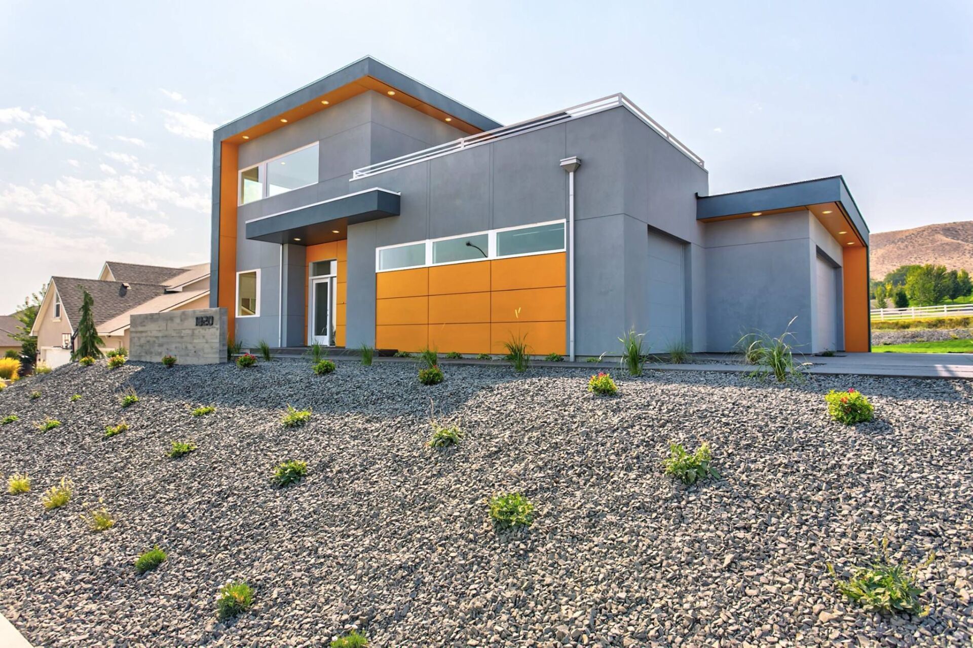 A modern house with a yellow garage door is sitting on top of a gravel hill.