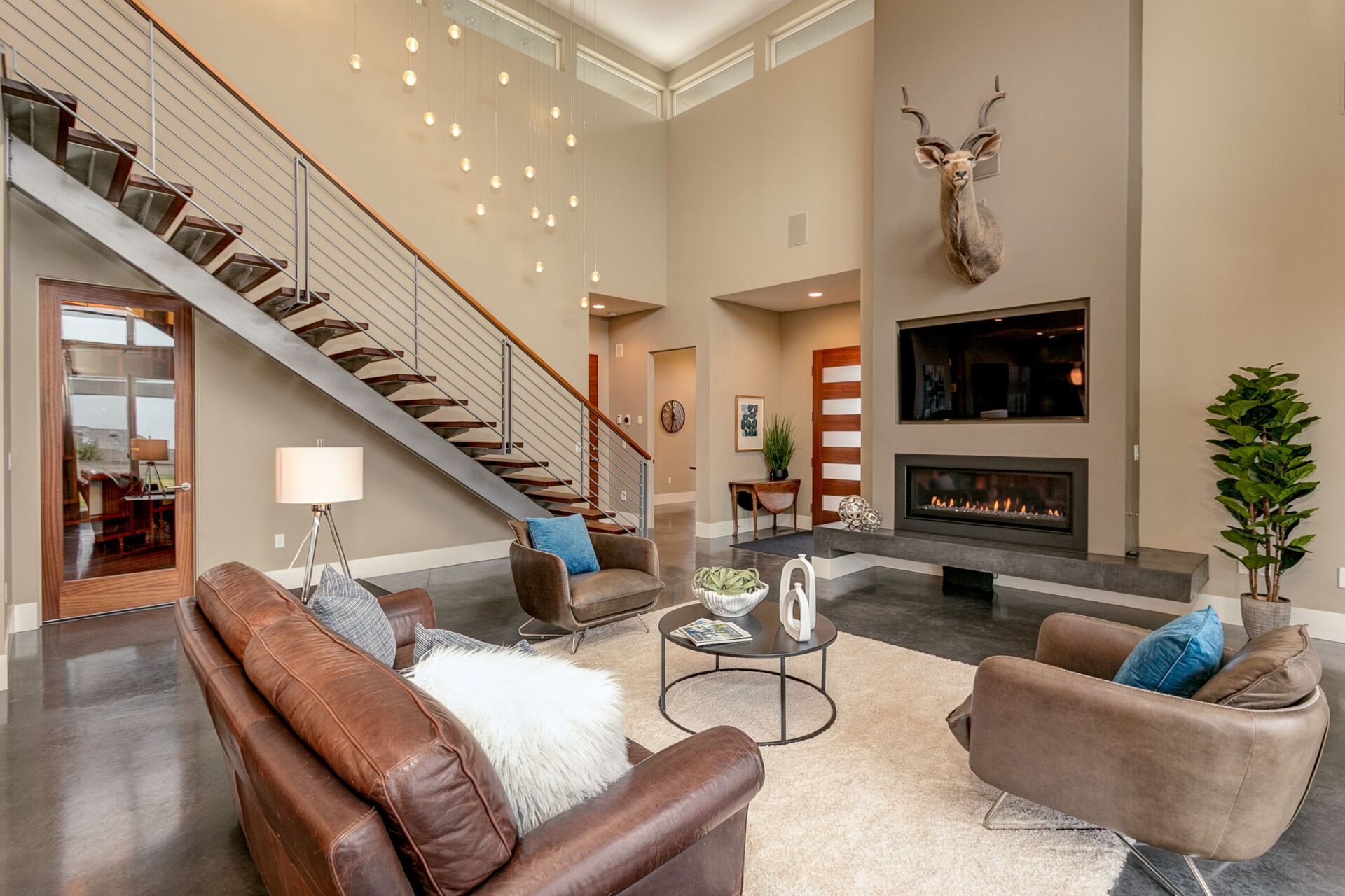 A living room with a staircase and a deer head on the wall.