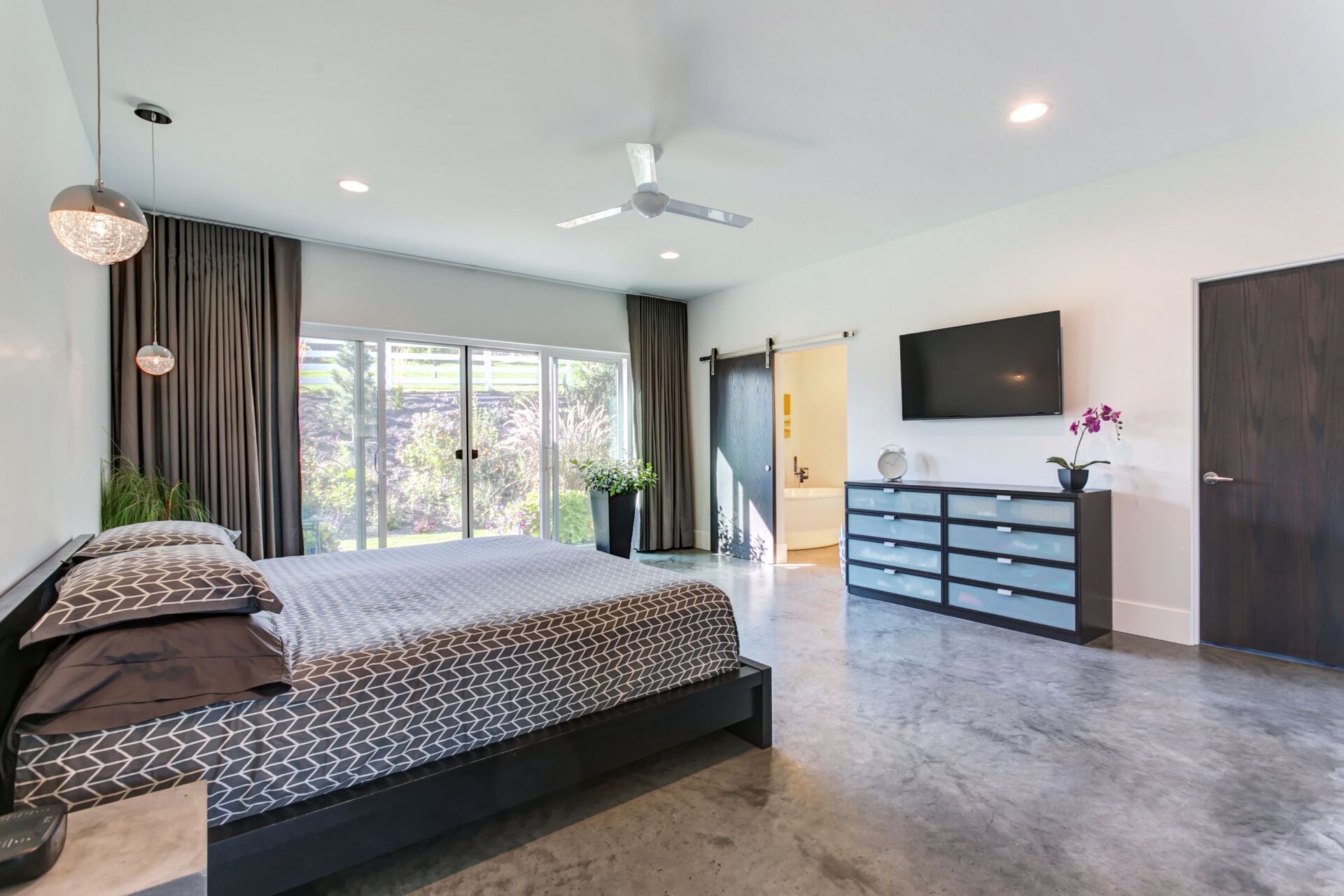 A bedroom with a large bed , dresser , television and a ceiling fan.