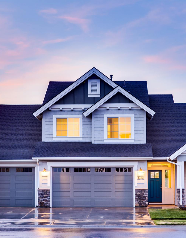 A large house with a blue roof and two garage doors is lit up at night.