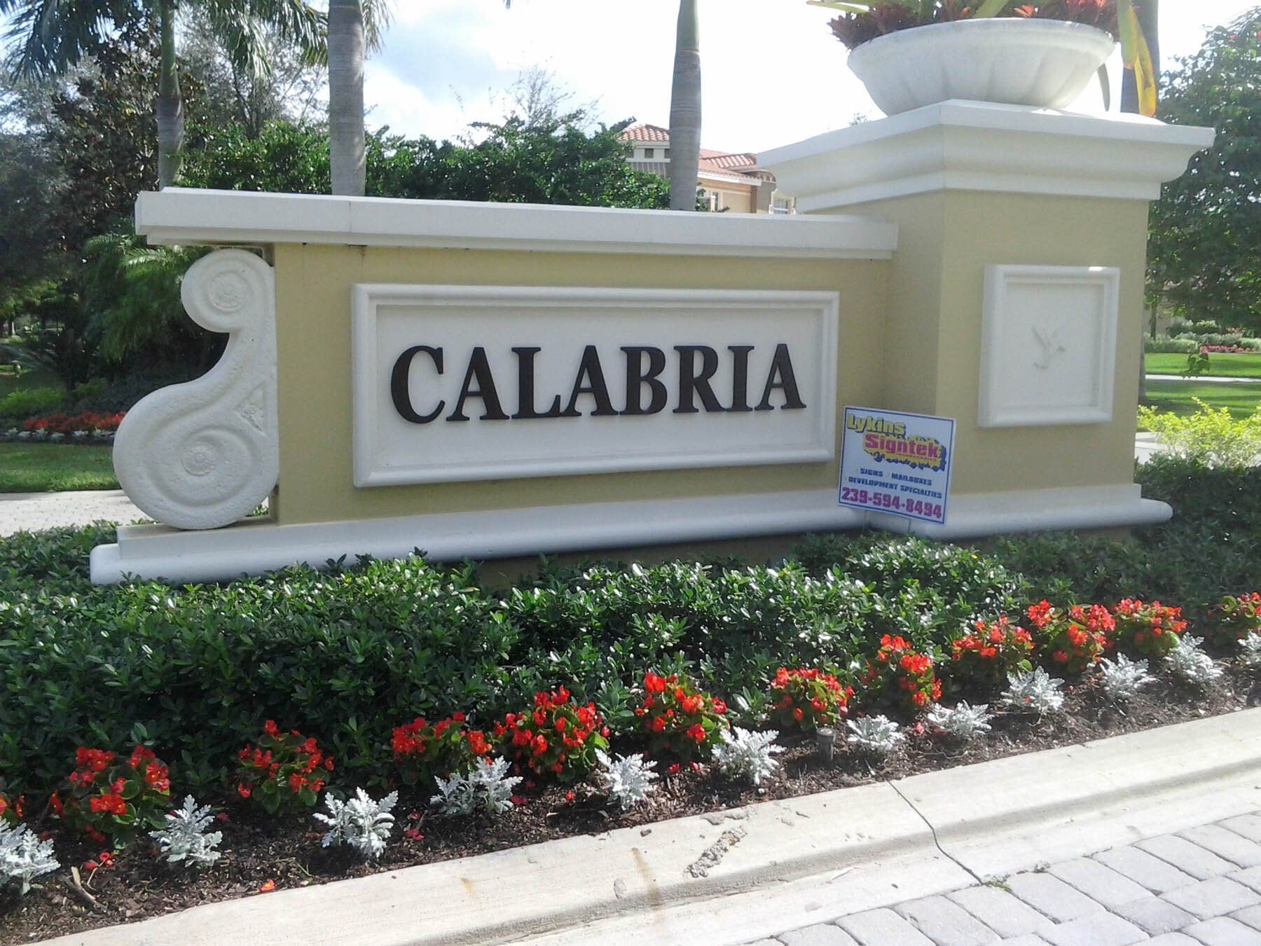 A sign for calabria is surrounded by flowers and bushes