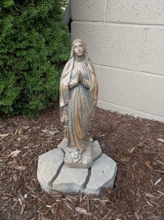 A statue of the virgin mary is sitting on top of a pile of mulch.