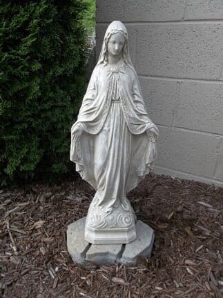 A statue of the virgin mary is standing on a rock in front of a building.